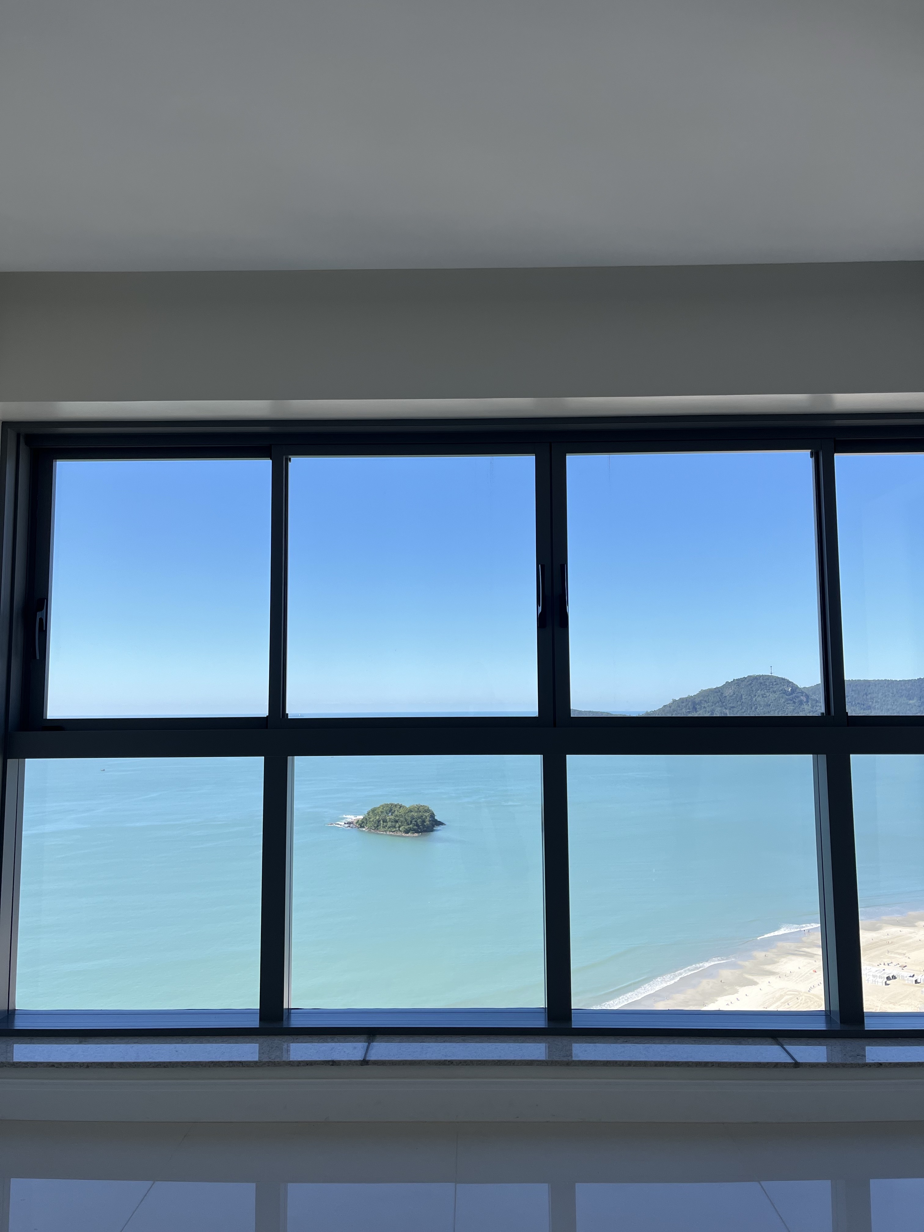 Janela do apartamento enquadrando a orla e a Ilha das Cabras